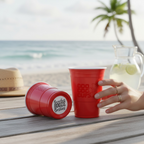 Red CooCoo Cups® with "Beaches Booze Besties" bottom stickers on a wooden surface by the ocean.