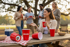 People enjoying a picnic with red "Oregon" CooCoo Cups®. One cup on the table shows a bottom stickers featuring a cool duck with sunglasses graphic.