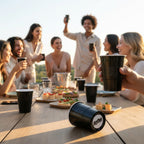 Group of people enjoying a outdoor gathering with black CooCoo Cups® and one cup laying on the table showing a bottom sticker featuring "BOOM" text.