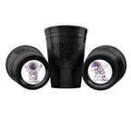 Three black CooCoo Cups® are shown. One displays the logo, while the other two lie on their sides, revealing bottom stickers featuring astronaut illustrations with peace-sign and dabbing poses.
