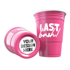Two pink CooCoo Cups® are shown. One displays the white text “Last Bash!” while the other lies on its side, revealing a customizable bottom sticker labeled “Your Design Here.”