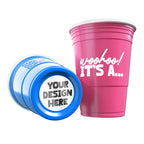 Two CooCoo Cups® are shown, one blue and one pink. One displays the white text “Woohoo! It's a...” while the other lies on its side, revealing a customizable bottom sticker labeled “Your Design Here.”