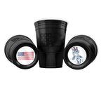 Three black CooCoo Cups® are shown. One stands upright displaying the logo, while the other two lie on their sides, revealing bottom stickers featuring a U.S. flag and a patriotic Uncle Sam pointing graphic.