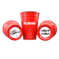 Three red CooCoo Cups® are shown. One displays "Florida" text, while the other two lie on their sides, revealing bottom stickers featuring gator imagery and “Chomp Chomp” designs.