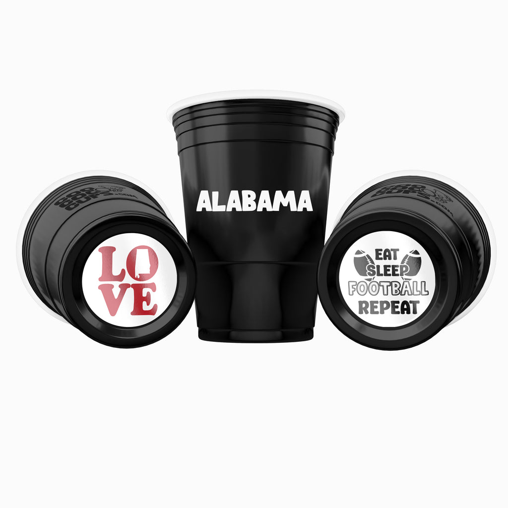 Three black CooCoo Cups® are shown. One displays "Alabama" text, while the other two lie on their sides, revealing bottom stickers featuring “LOVE” with Alabama state icon and a "Eat, Sleep, Football, Repeat" graphic.